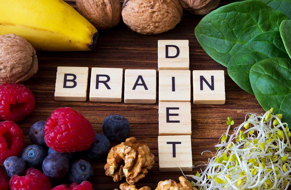 Wooden letter tiles spelling 'BRAIN DIET' surrounded by fruits, nuts, spinach, and sprouts on a wooden surface.