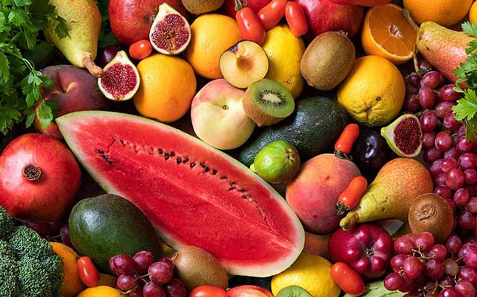 Assorted fresh fruits and vegetables, including watermelon, carrots, broccoli, figs, citrus fruits, apples, grapes, and parsley.