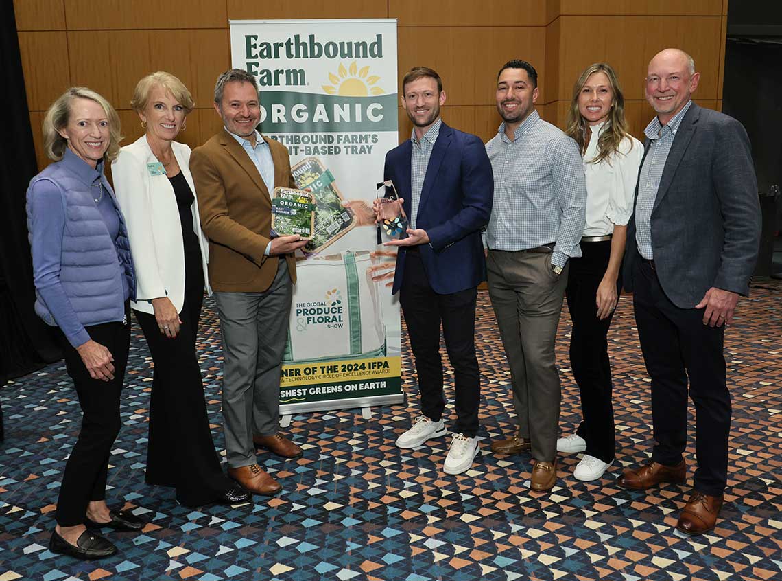 A group of seven people poses with Earthbound Farm Organic products and award in front of a branded banner.