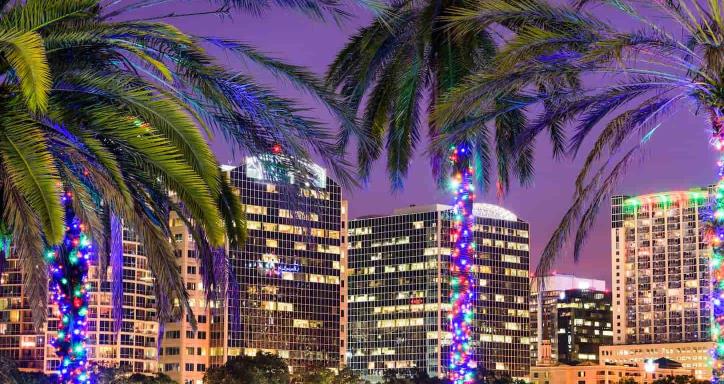 Orlando, Florida, USA downtown skyline at Eola Lake with palm trees wrapped in colorful lights.