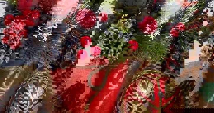 Festive Christmas arrangement with pine branches, berries, flowers, and decorations in a red pot.