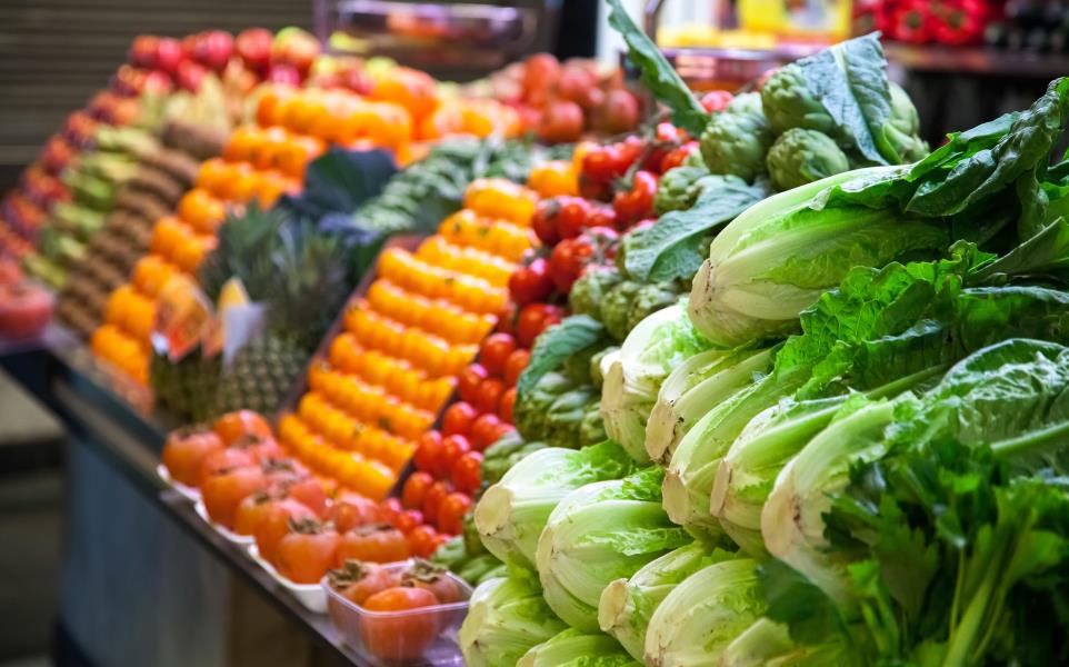 Produce marketplace aisle with an assortment of vegetables. Nearest being romaine lettuce and then other colorful produce going down the aisle